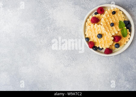 Waffle ondulato i cookie con lamponi freschi e mirtilli su un sfondo di calcestruzzo. Spazio di copia Foto Stock