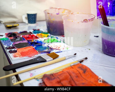 Strumenti di artista, pennelli, bianco secchio di acqua e di acido acrilico colore tavolozza artista sulla tavola in arte studio. Foto Stock