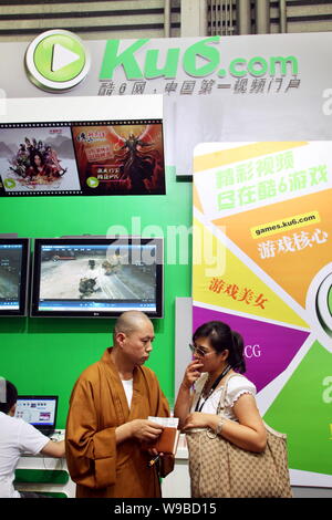 Un monaco cinese parla con una donna allo stand di Ku6.com durante l'ottava China Digital Entertainment Expo e conferenza, noto come ChinaJoy 2010, in S Foto Stock