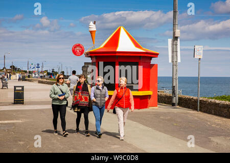 In Irlanda, il Leinster, Fingal, Portmarnock, gruppo di quattro femmine i visitatori a piedi sul lungomare passato gelato in stallo Foto Stock