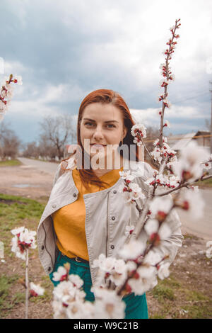 I Capelli rossi ragazza in una molla giardino fiorito. Rami della molla di fioritura cherry macro con soft focus. Bella immagine floreale di primavera la natura panor Foto Stock