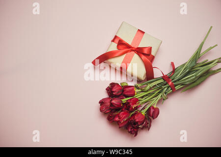 Piano di composizione laici bouquet di tulipani rossi con confezioni regalo nastro di raso su sfondo rosa con lo spazio vuoto al centro, vista dall'alto Foto Stock