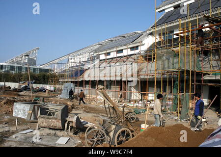 Costruzione cinese i lavoratori sono visti i ponteggi per installare il calore solare tubo collettori e pannelli solari sul tetto di un edificio in Val solare Foto Stock