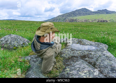 Stanco viaggiatore in montagna - un uomo in un cappello e camp vestiti in appoggio, fissando in distanza, giacente su di un altopiano di montagna Foto Stock