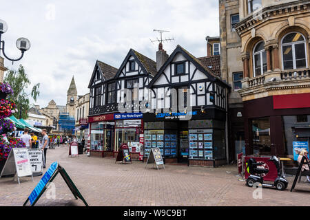 3 negozi su Fore Street Trowbridge in una simulazione di edificio Tudor con il giorno di mercato gli operatori visibile in strada Foto Stock