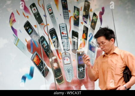 --FILE--un uomo cinese guardando un breve messaggio sul suo telefono mobile a piedi passato un annuncio per i telefoni cellulari in Cina a Shanghai, 17 luglio 2007. Foto Stock