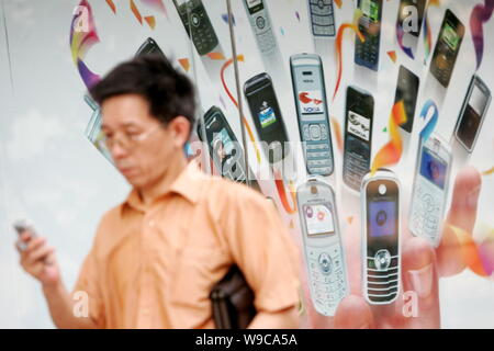 --FILE--un uomo cinese guardando un breve messaggio sul suo telefono mobile a piedi passato un annuncio per i telefoni cellulari in Cina a Shanghai, 17 luglio 2007. Foto Stock