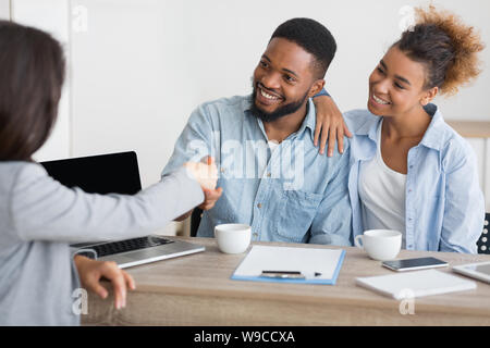 Sorridente afro handshaking di coniugi con broker assicurativo in office Foto Stock