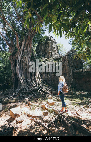 Caucasian donna bionda scoprendo le rovine di Angkor Wat tempio complesso in Siem Reap, Cambogia. Albero che cresce sul tetto del tempio cancello di ingresso arc Foto Stock