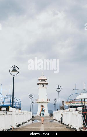 Donna che cammina sul molo verso il bianco faro in Baan Bang Bao fisherman village su Koh Chang island, Thailandia. Orientamento verticale Foto Stock