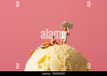 Alcune persone in miniatura di indossare il costume da bagno rilassante per un gelato sfera, contro un sfondo rosa con qualche spazio vuoto intorno a loro Foto Stock