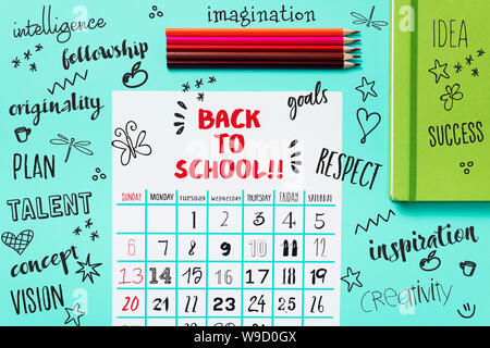 Elevato angolo di visione di un calendario con il testo torna a scuola su un tavolo blu, accanto ad alcune matite di diversi colori e un verde notepad e s Foto Stock