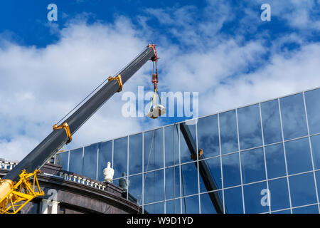 Il braccio telescopico di una costruzione gru solleva il carico contro la parete a specchio dell'edificio riflette il cielo Foto Stock