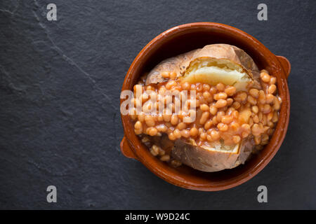 Un jacket potato che è stata cotta in un forno di alogeno è servito per il pranzo con una porzione di fagioli in una ciotola. Sfondo di ardesia. Il Dorset England Regno Unito GB Foto Stock