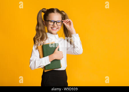 Scuola felice ragazza con libri su sfondo giallo, studio shot Foto Stock