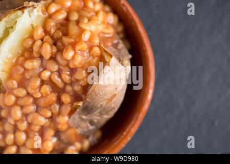 Un jacket potato che è stata cotta in un forno di alogeno è servito per il pranzo con una porzione di fagioli in una ciotola. Sfondo di ardesia. Il Dorset England Regno Unito GB Foto Stock