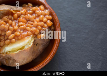 Un jacket potato che è stata cotta in un forno di alogeno è servito per il pranzo con una porzione di fagioli in una ciotola. Sfondo di ardesia. Il Dorset England Regno Unito GB Foto Stock