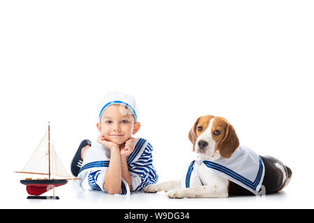 Preschooler sorridente bambino in sailor suit con nave giocattolo e cane beagle su bianco Foto Stock