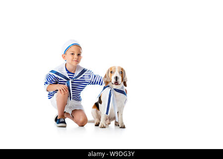 Preschooler sorridente bambino in costume da marinaio e cane beagle su bianco Foto Stock