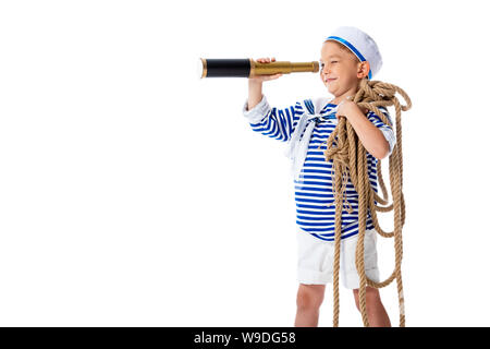 Preschooler sorridente bambino in costume da marinaio cercando in il cannocchiale e tenendo la corda isolato su bianco Foto Stock