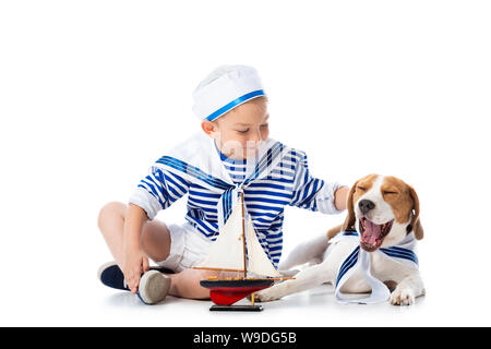 Preschooler bambino in sailor suit con nave giocattolo e cane beagle su bianco Foto Stock