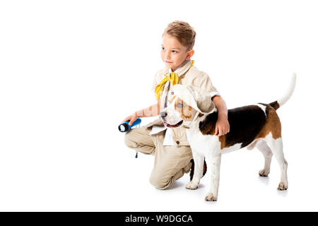 Sorridente explorer bambino abbracciando simpatico cane beagle in hat e tenendo la torcia elettrica su bianco Foto Stock