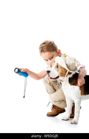 Sorridente explorer bambino tenendo la torcia elettrica e abbracciando il cane beagle in hat su bianco Foto Stock