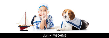 Panoramica del ragazzo in sailor suit con nave giocattolo e cane beagle su bianco Foto Stock