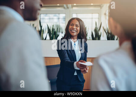 Sorridente African American concierge in piedi dietro un banco di ricevimento di dare informazioni sulle camere a due gli ospiti che arrivano in hotel Foto Stock