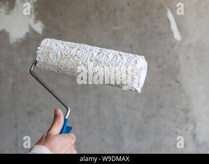 Un pittore dipinge un muro di cemento con vernice bianca, un maschio di  mano con un rullo di vernice per la verniciatura di una parete Foto stock -  Alamy