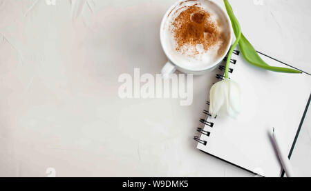 Sullo sfondo di un area di lavoro di ispirazione con caffè cosparsi di cannella. fiore bianco e notebook per le idee creative sulla superficie bianca. Foto Stock