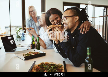 Due ridere i giovani Americani africani imprenditori aventi la pizza e le birre con i colleghi in un ufficio dopo il lavoro Foto Stock