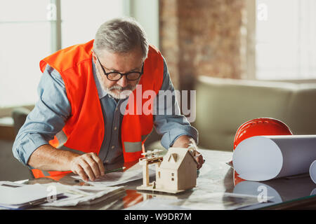 Close up photoshot maschile di architetto e ingegnere fare un modello della futura casa per giovani della famiglia. Uomo che lavora in ufficio con miniatura, disegni, cianografia. Prima Casa, industriale, building concept. Foto Stock