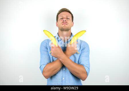 Giovane uomo bello trattenere due banane fresche nelle sue mani incrociate isolato su sfondo bianco Foto Stock
