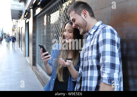Felice coppia controllo sorprendente smart phone contenuto in piedi in strada Foto Stock