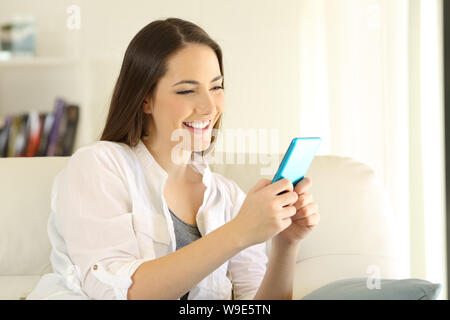 Donna felice utilizza smart phone seduta su un divano nel salotto di casa Foto Stock