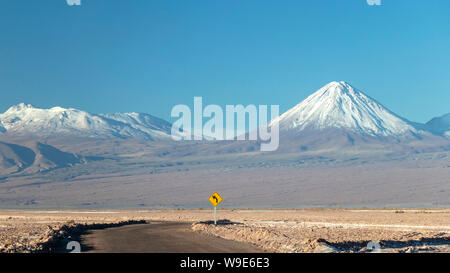 Strada del deserto di Atacama: cartello giallo con freccia curva e Snow capped mountain sullo sfondo nel deserto di Atacama, Cile, Sud America Foto Stock