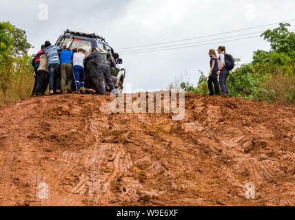 Gli studenti di un fieldtrip in Malawi spingere un veicolo a filamento di una strada fangosa Foto Stock