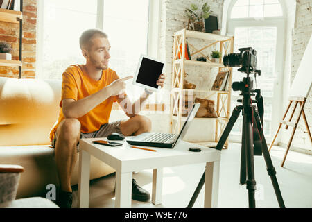 Giovane maschio caucasico blogger con telecamera professionale la registrazione video recensione del tablet a casa. Blogging, videoblog, vlogging. L'uomo facendo vlog o live stream su foto o novità tecniche. Foto Stock