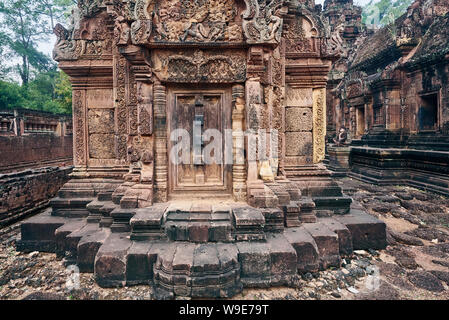 Porta cieca, ringhiere e devatas scavate nella pietra arenaria rossa pareti di Banteay Srei area del tempio di Angkor a Siem Reap, Cambogia Foto Stock