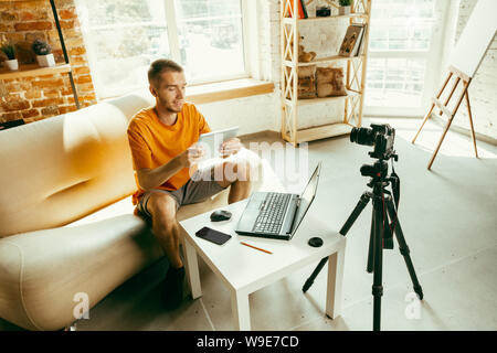 Giovane maschio caucasico blogger con telecamera professionale la registrazione video recensione del tablet a casa. Blogging, videoblog, vlogging. L'uomo facendo vlog o live stream su foto o novità tecniche. Foto Stock