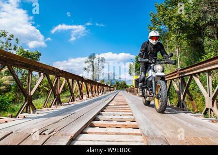 L uomo alla guida della sua scrambler motocicletta del tipo sopra ponte temporaneo Foto Stock