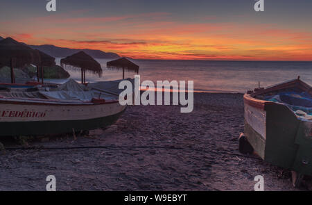 Nerja, Malaga, Andalusi, Spagna - 27 Gennaio 2019: due barche da pesca bloccati sulla spiaggia in un'alba con cielo rossastro Foto Stock