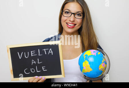 Latino femmina giovane insegnante holding globe e lavagna con spagnolo scritto "Vuelta al cole' (torna a scuola). Foto Stock