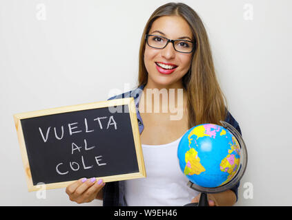 Latino femmina giovane insegnante holding globe e lavagna con spagnolo scritto "Vuelta al cole' (torna a scuola). Foto Stock