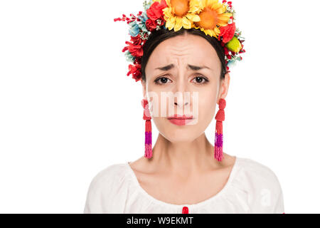 Sconvolto bruna giovane donna in nazionale ucraino camicia ricamata e ghirlanda floreale isolato su bianco Foto Stock