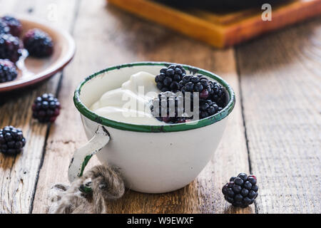 Sana colazione o brunch, preferito pasto mattutino con frutti di bosco. Yogurt freschi estate more nelle zone rurali la tazza sul tavolo di legno, close up, selettivo f Foto Stock