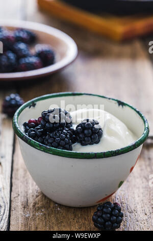 Sana colazione o brunch, preferito pasto mattutino con frutti di bosco. Yogurt freschi estate more nelle zone rurali la tazza sul tavolo di legno, close up, selettivo f Foto Stock