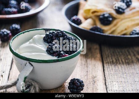 Sana colazione o brunch, preferito pasto mattutino con frutti di bosco. Yogurt freschi estate more nelle zone rurali la tazza sul tavolo di legno, close up, selettivo f Foto Stock