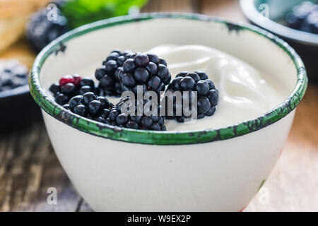 Sana colazione o brunch, preferito pasto mattutino con frutti di bosco. Yogurt freschi estate more nelle zone rurali la tazza sul tavolo di legno, close up, selettivo f Foto Stock